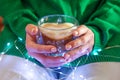 Woman with glass cup of coffee with milk. Christmas lights. Heart shape. Close-up Royalty Free Stock Photo
