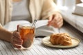 Woman with glass cup of tasty aromatic tea reading book at table, closeup Royalty Free Stock Photo