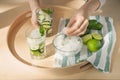 Woman with glass of fresh cucumber water taking ice cube from bowl on tray Royalty Free Stock Photo