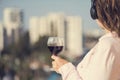 Woman with glass of wine listening music in a headphones against the background of town at summer