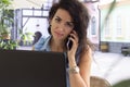 Woman in glass working remotely with laptop and phone in cafe. Beautiful brunette using notebook in cafe. Happy businesswoman call Royalty Free Stock Photo