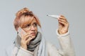 Woman in glasses caught cold, looking at thermometer, calling a doctor. flu season concept Royalty Free Stock Photo