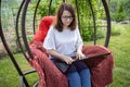 Woman with glasses with long hair typing on a laptop while sitting in a nest chair