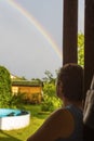 A woman with glasses, on an open terrace looking at the rainbow