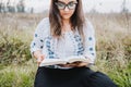 Woman with glasses sitting outdoor on the grass holding and reading an open Bible. Selective focus. Royalty Free Stock Photo