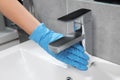 Woman in glove cleaning faucet of bathroom sink with paper towel, closeup