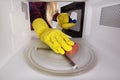 Woman in gloves with sponge and spray bottle cleaning microwave.