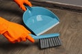 Woman in gloves sweeping wooden floor with plastic whisk broom and dustpan indoors, closeup Royalty Free Stock Photo