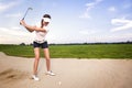 Woman golfer in sand trap preparing to hit ball.