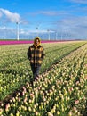 A woman gracefully stands in a vibrant field of tulips, surrounded by bursts of colorful petals under the Dutch windmill Royalty Free Stock Photo