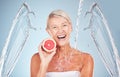 Woman, grapefruit and studio portrait with water splash, happiness and cosmetics for wellness by blue background. Senior