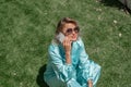 Woman grass. Happy woman with blond curly hair in glasses and in a blue overalls sits on the summer fresh green grass