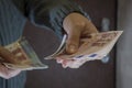 Woman`s hands in gray knit sweater hold out three ten-euro bills against brown front door