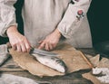 woman in gray linen clothes cleans the fish sea bass scales on a brown wooden board Royalty Free Stock Photo