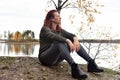 Woman in gray sits on stones by the lake in autumn