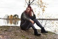 Woman in gray sits on stones by the lake in autumn