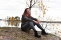 Woman in gray sits on stones by the lake in autumn