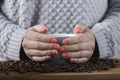 Woman in gray sweater holding a cup of coffee in her hands and roasted coffee on a wooden table Royalty Free Stock Photo