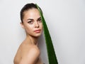 woman with green aloe leaf on light background cropped view naked shoulders clean skin