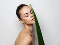 woman with green aloe leaf on light background cropped view naked shoulders