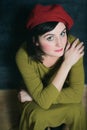 Woman in green dress and red beret sitting near the black wall