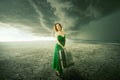 Woman in green dress with suitcase standing alone in the middle of the desert