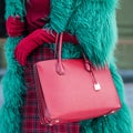 A woman in a green furry and warm fur coat in autumn or winter. Red burgundy bag. Fashionable bag close-up in female hands. Royalty Free Stock Photo