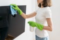 Woman in green gloves with spray bottle wipe tv screen in room Royalty Free Stock Photo