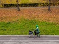 A woman in green overalls carries plastic bags in a shopping cart. Housing and communal services janitor at work