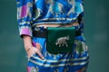 Woman with green satin bag with silver elephant and blue silk trousers and shirt before Emporio Armani