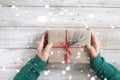 A woman in a green sweater holding a Christmas gift with a red ribbon and snow over on a wooden table. Royalty Free Stock Photo