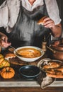 Woman in grey apron mixing cream with pumpkin cream soup Royalty Free Stock Photo