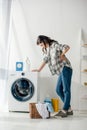 woman in grey shirt and jeans standing near washer woman and holding backache Royalty Free Stock Photo