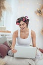 Woman in hair curlers sitting on bed with laptop Royalty Free Stock Photo