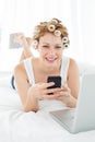 Woman in hair curlers text messaging by laptop in bed Royalty Free Stock Photo