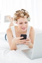 Woman in hair curlers text messaging by laptop in bed Royalty Free Stock Photo