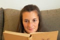 Woman with a half smile enjoys while reading a book in concentration that she holds in her hands