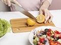 A woman halves a lemon on a cutting Board to add lemon juice to a Greek salad