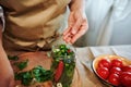 Woman hand adding peppercorns in glass jarfilles with stacked fresh chili peppers while making preserves at home kitchen