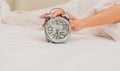 Woman hand on alarm clock, Wake up concept. White bed background.