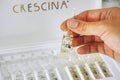 Woman hand with ampoule of Crescina Re-Growth in front of Crescina treatment box