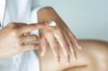 Woman hand applying cream or lotion on hand lying on white bed, selective focus