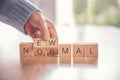 Woman hand arranging wooden cubes with NEW NORMAL word.