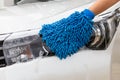 Woman hand with blue microfiber fabric washing headlight modern car or cleaning automobile.