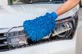 Woman hand with blue microfiber fabric washing headlight modern car or cleaning automobile.