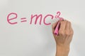 Woman hand with bright pink chalk writing mass-energy equivalence formula on white desk or wall