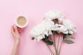 Woman hand with cup of coffee and beautiful white peony flowers on pink pastel table top view. Cozy breakfast in flat lay style. Royalty Free Stock Photo