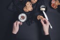 Woman hand with cup of coffee or cappuccino and chocolate cookies, biscuits on black table background. Afternoon break time. Break Royalty Free Stock Photo