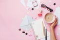 Woman hand with cup of coffee, macaron, office supply and empty notebook on pink pastel table top view. Flat lay style.