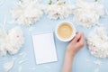 Woman hand with cup of coffee, open notebook and beautiful white peony flowers on pastel table. Cozy breakfast. Flat lay Royalty Free Stock Photo